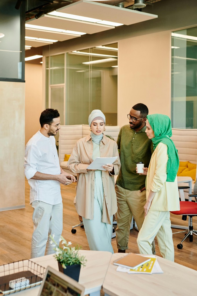 Four diverse colleagues standing together reviewing a document in a bright open-plan office.